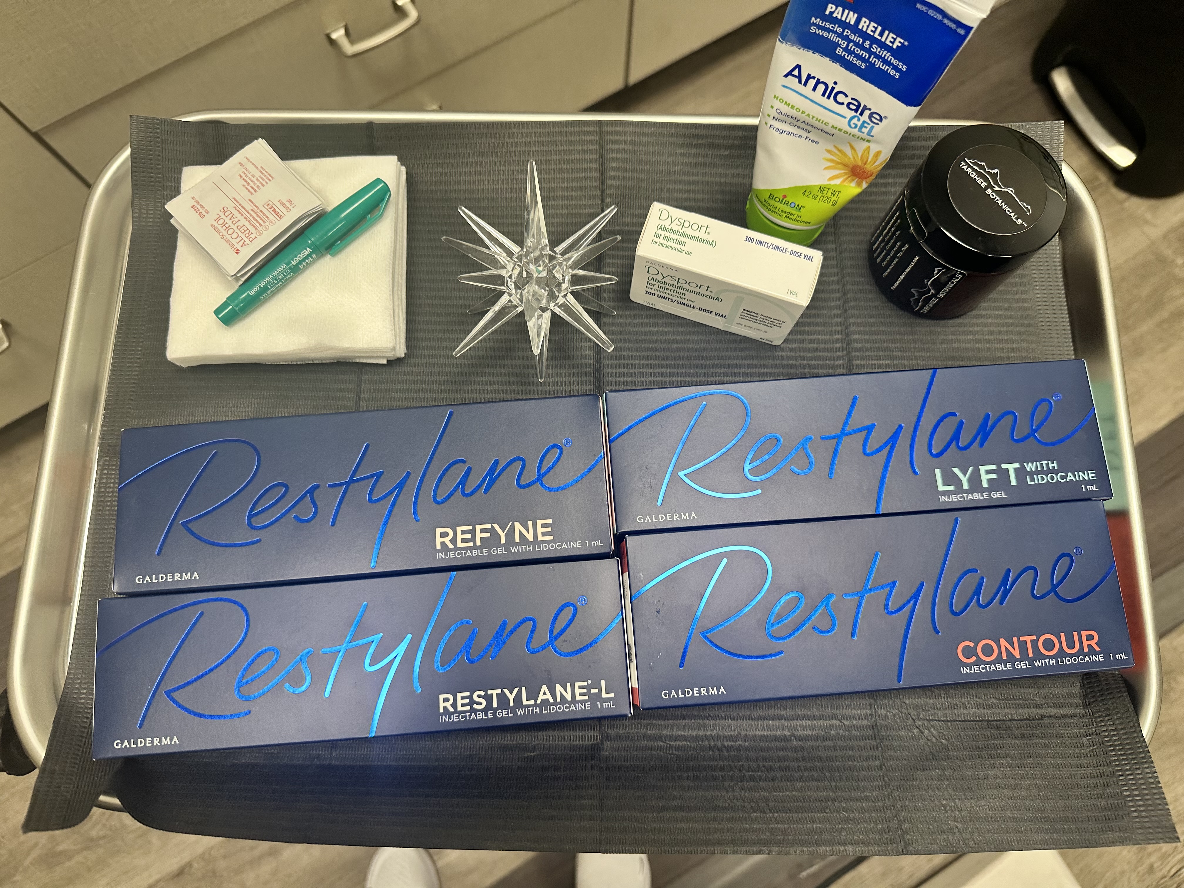 Tray of dermal filler product boxes and supplies arranged on a clinic cart.
