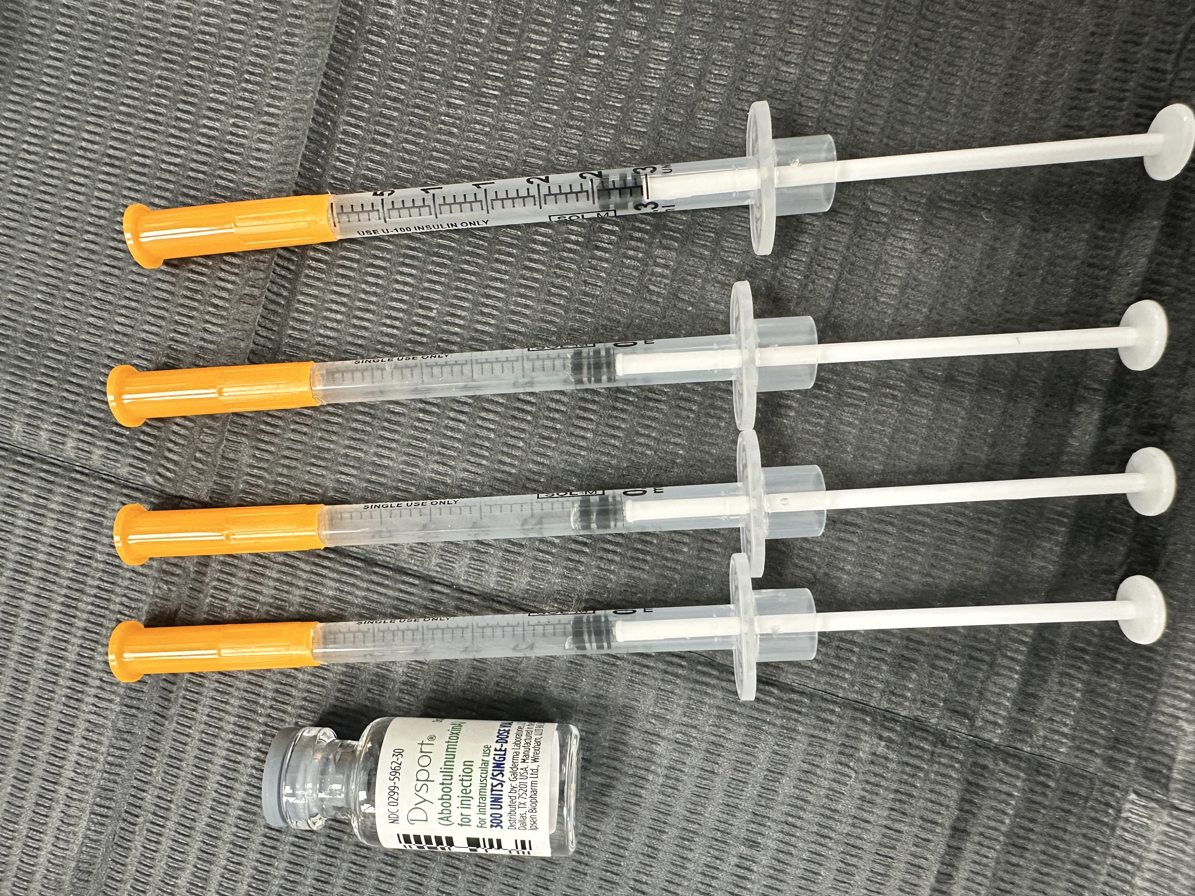 Vial of a neuromodulator product with prepared syringes on a clinic tray.