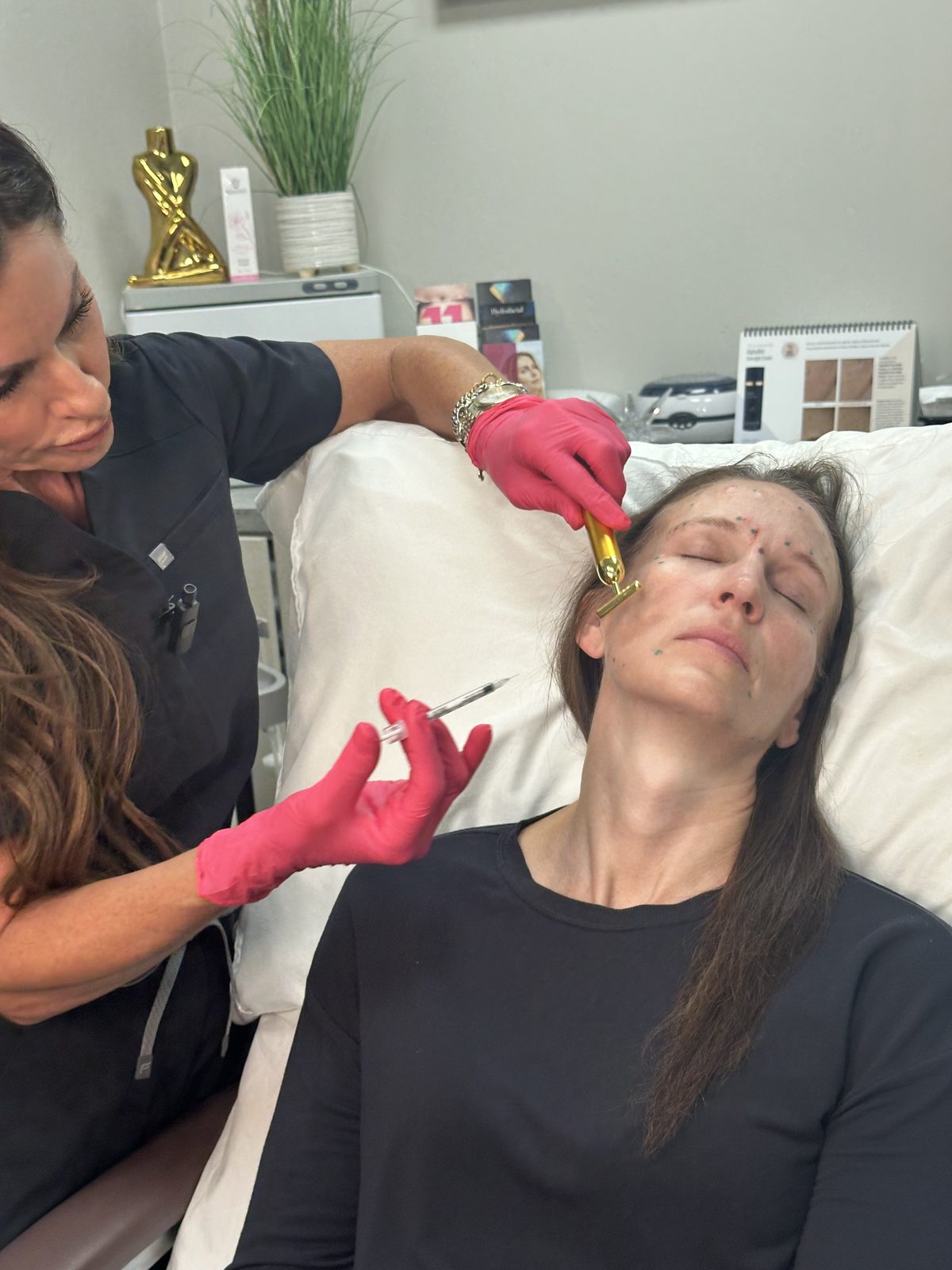 Candid in-room shot of a provider in pink gloves performing a facial injectable procedure on a reclined client